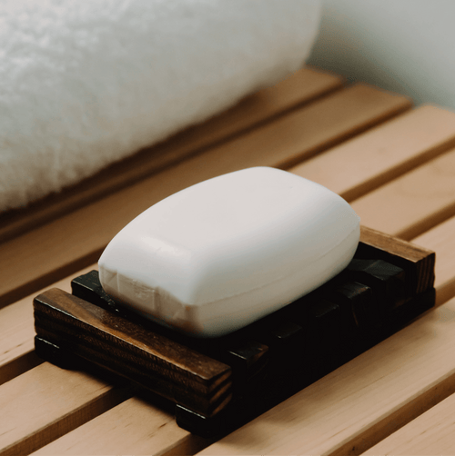 Bar of soap on a wooden soap dish with a towel in the background